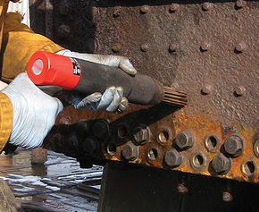 Needle scaler removing rust around bolts on ship deck